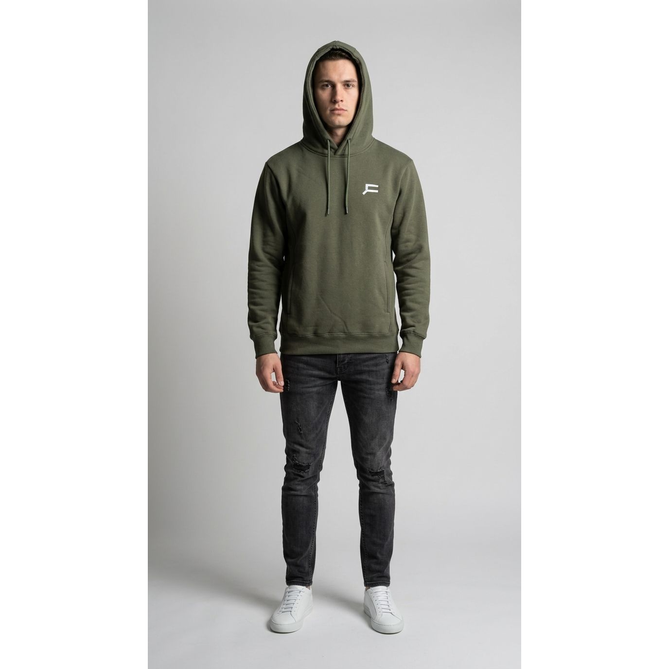 Person wearing an olive green hoodie with a logo on a gray background