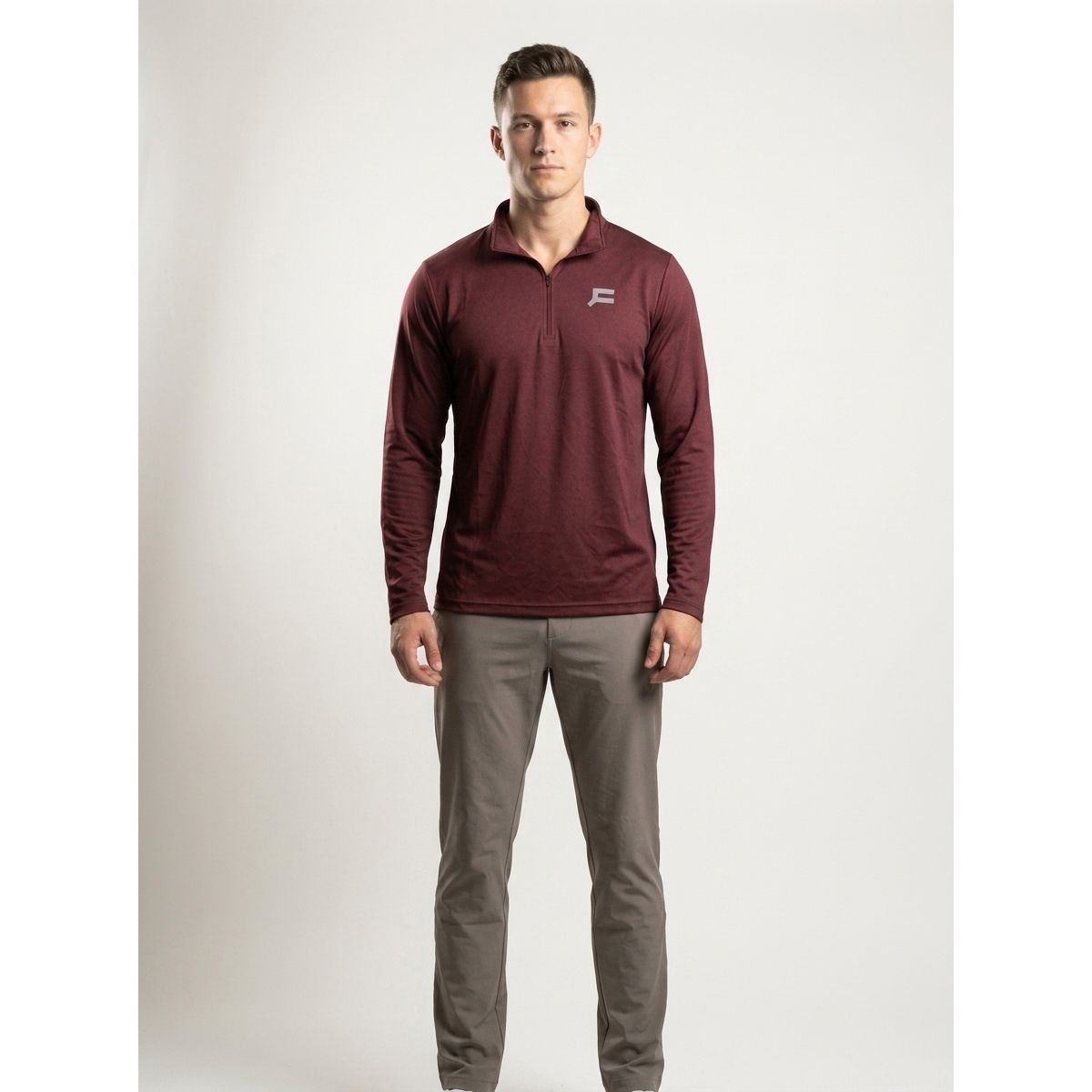 A man modeling a long-sleeve quarter-zip pullover in maroon with a small white logo on the left chest, paired with gray pants, against a light gray studio background.