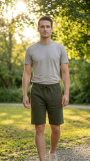 Man wearing a gray t-shirt and olive green shorts standing outdoors with trees in the background