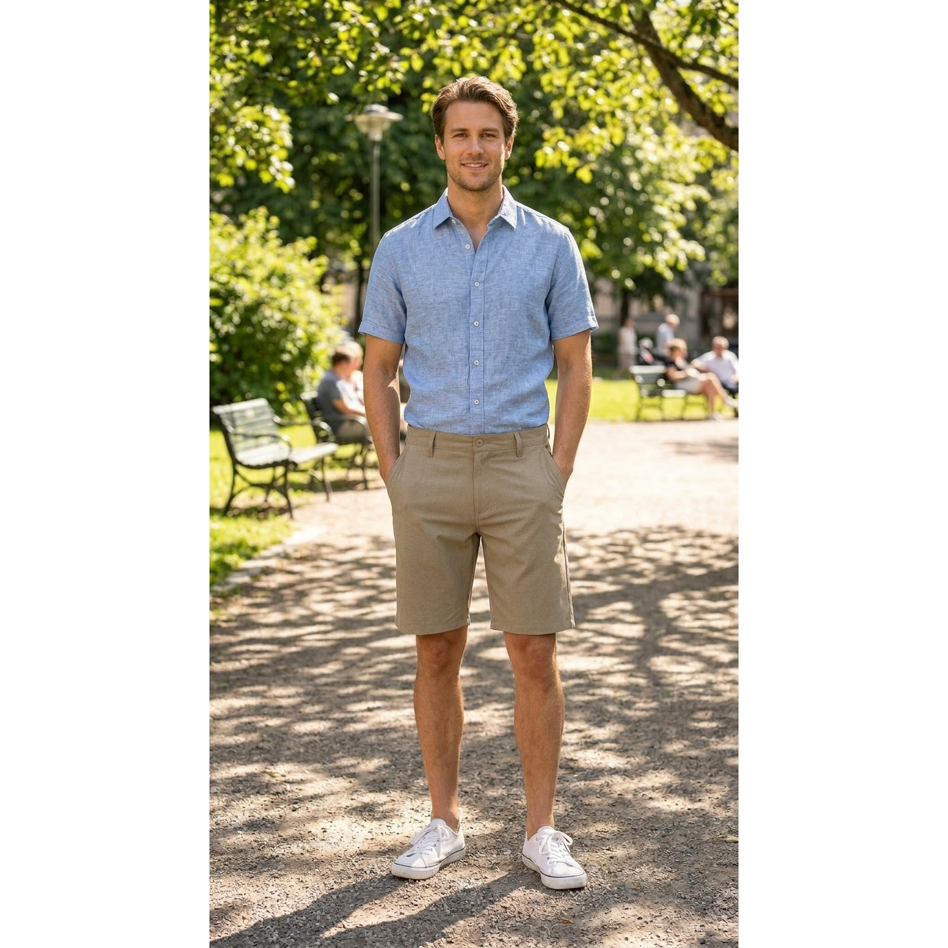 Man wearing a light blue shirt and beige shorts standing in a park.