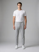 A man modeling a white crew-neck t-shirt and light gray sweatpants against a neutral gray studio background.