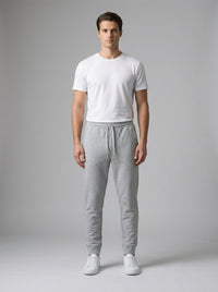 A man modeling a white crew-neck t-shirt and light gray sweatpants against a neutral gray studio background.